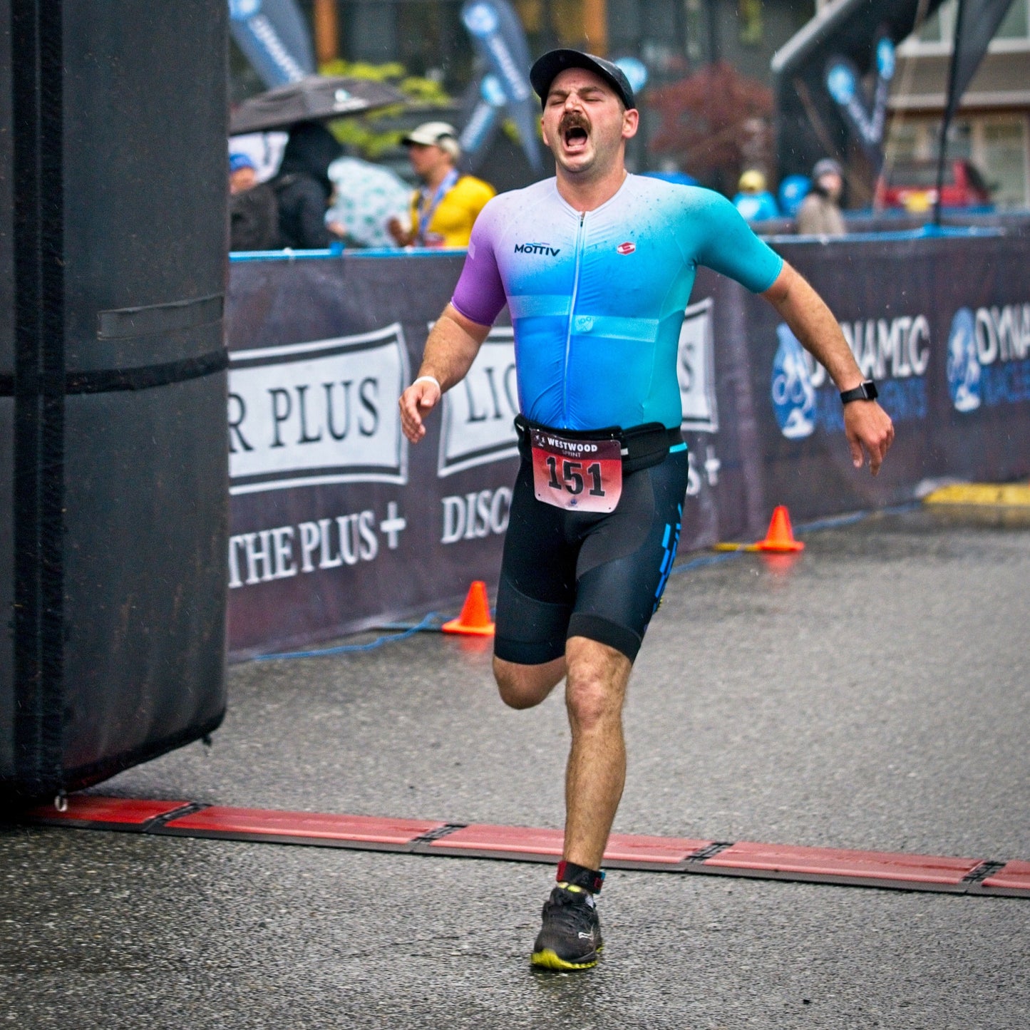 Man yelling hurray while crossing a finish line of a running race, wearing a triathlon suit